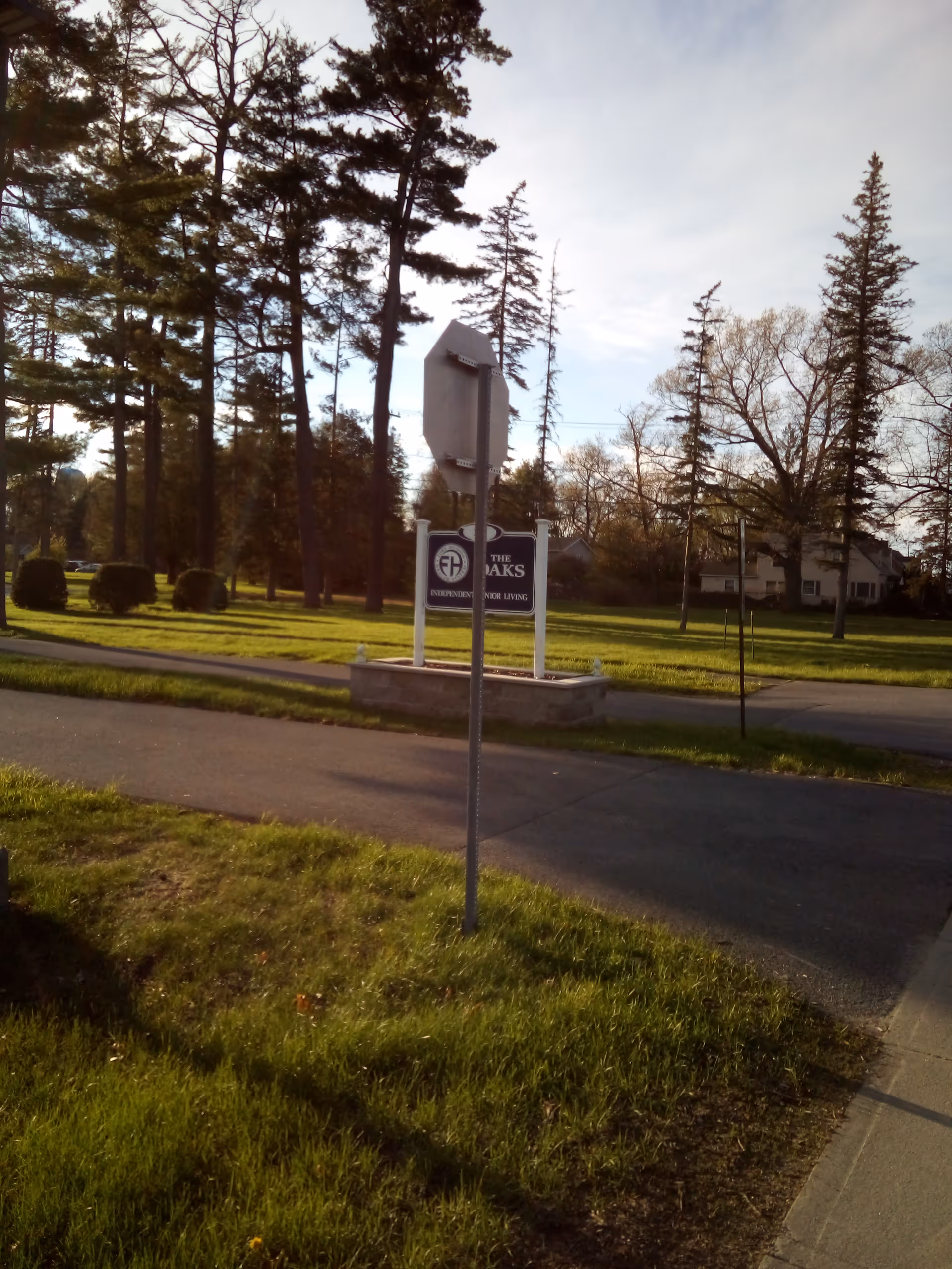 Outdoor scene with a Fort Hudson Health System sign along a road near trees and grass.