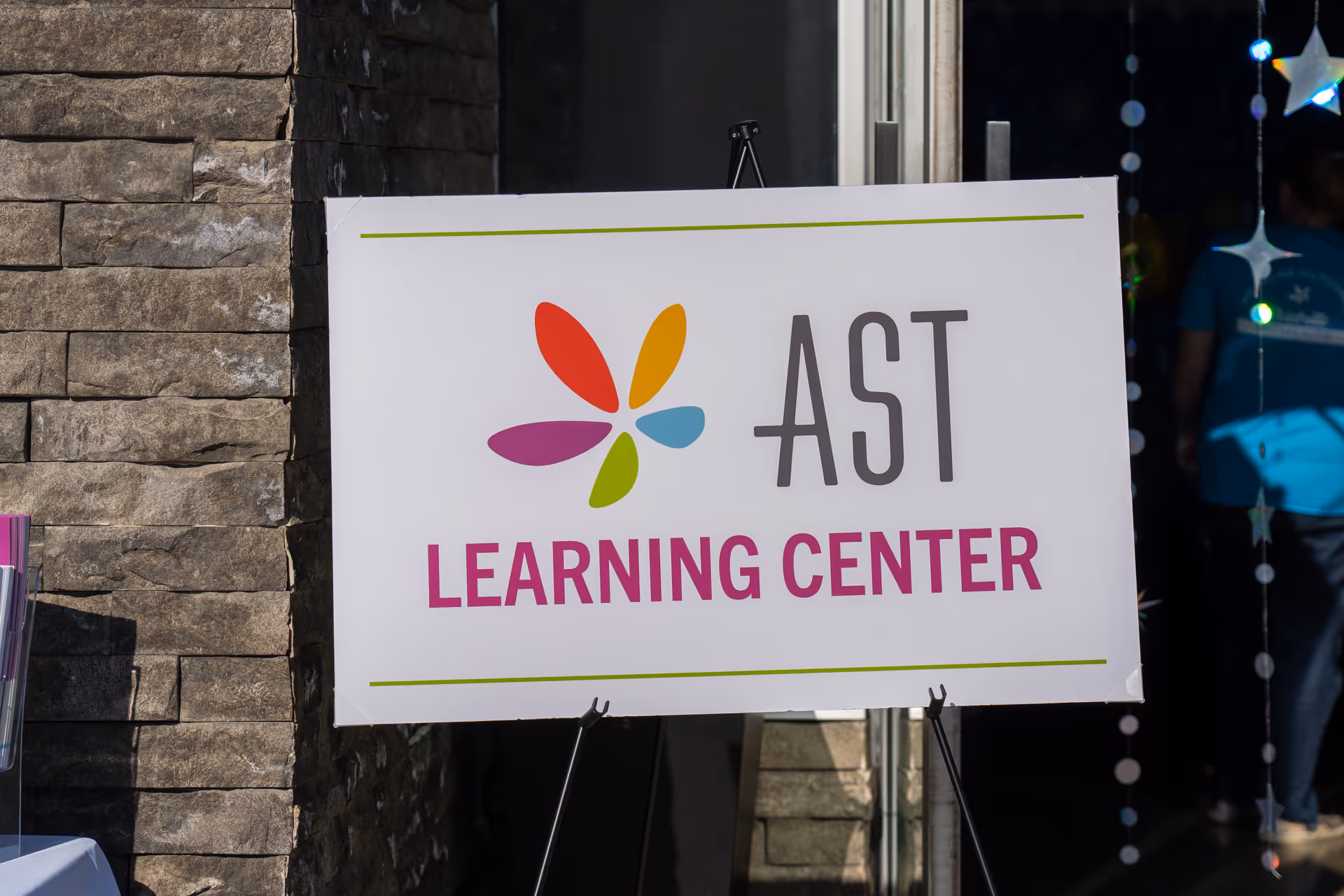 Outdoor sign reading AST Learning Center with colorful logo beside a stone building.