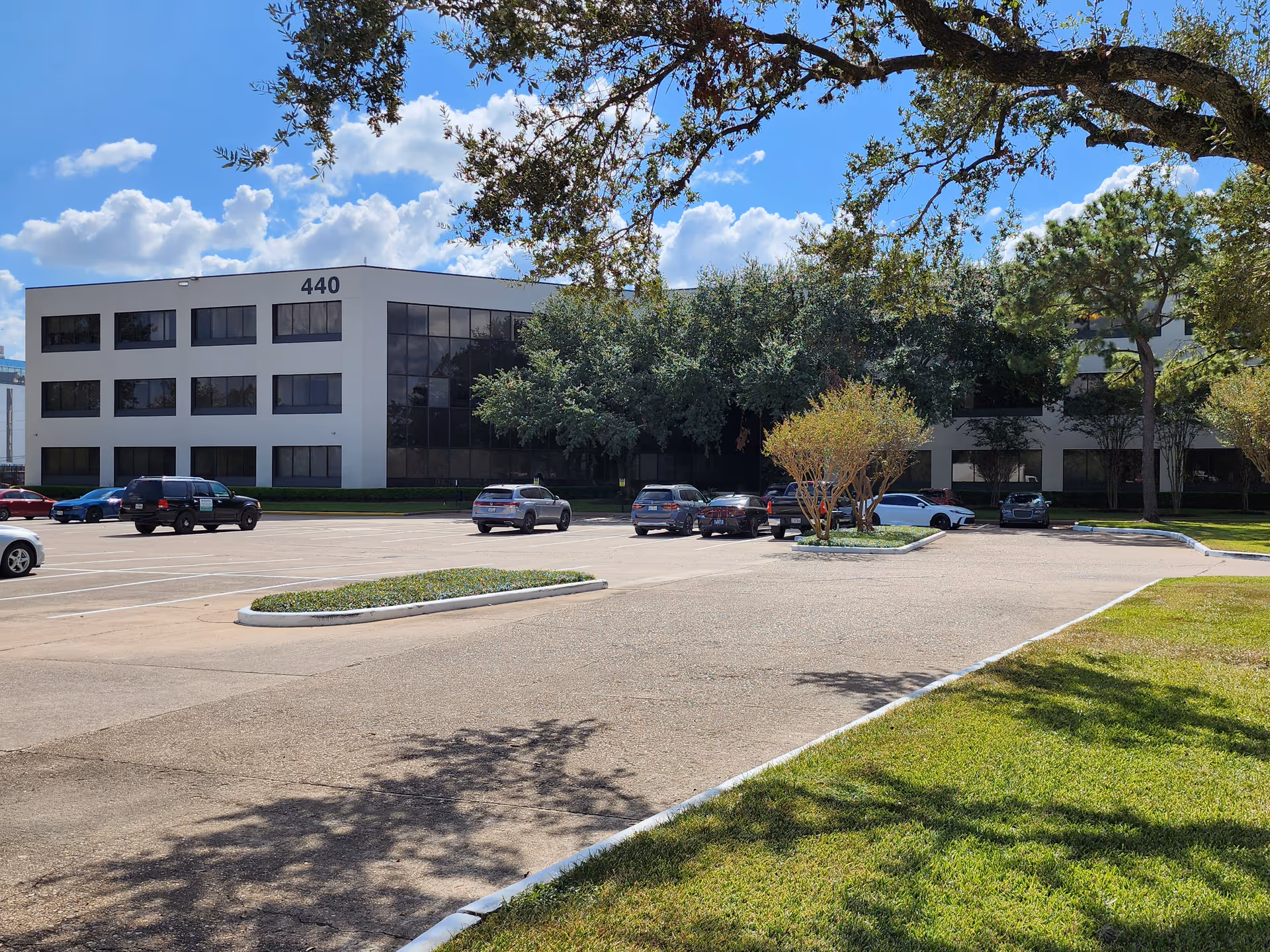 Front view of a white, multi-story building with a parking lot and trees.