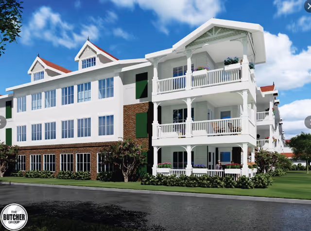 Front exterior of a multi-story white senior living building with wraparound porches and balconies and a lawn under a blue sky.