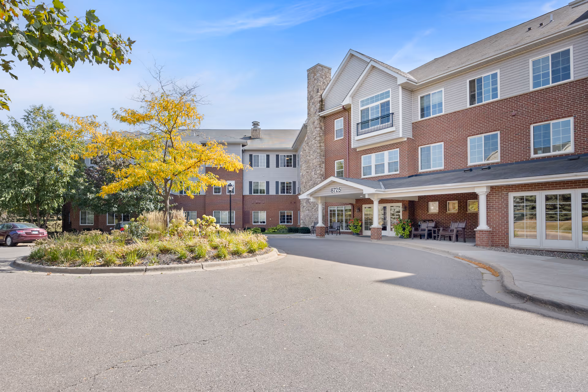 Entrance of a three-story brick senior living building with a covered porte-cochère, circular driveway, and landscaped island.