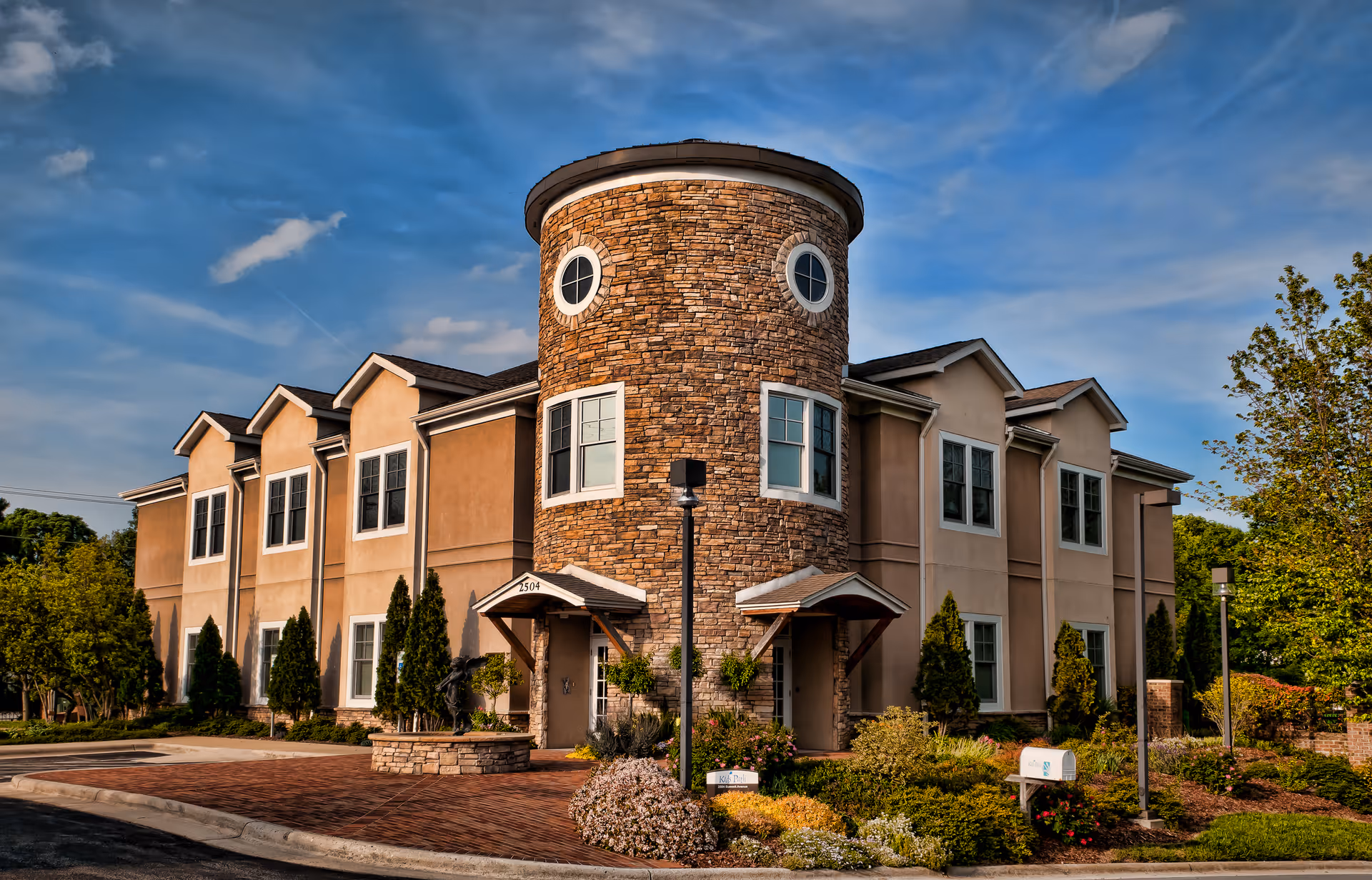 Exterior view of a multi-story senior living facility with a round stone tower and landscaped entrance.