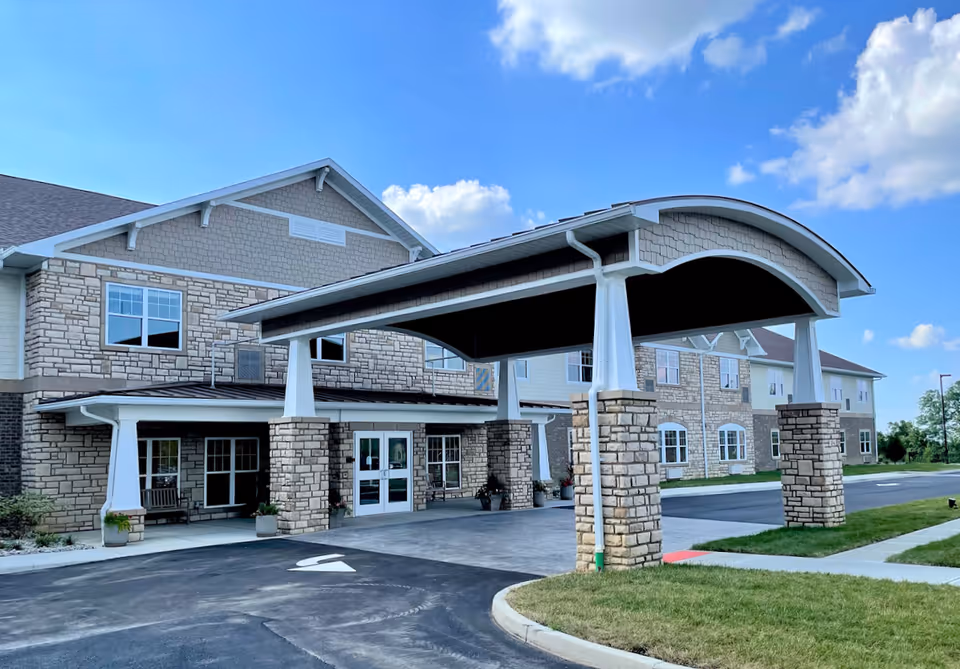 Front entrance of a stone-clad senior living building with a covered porte-cochère and driveway.