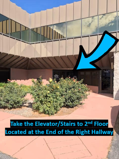 Exterior view of a senior living facility entrance with walkway, shrubs, and a large blue arrow.