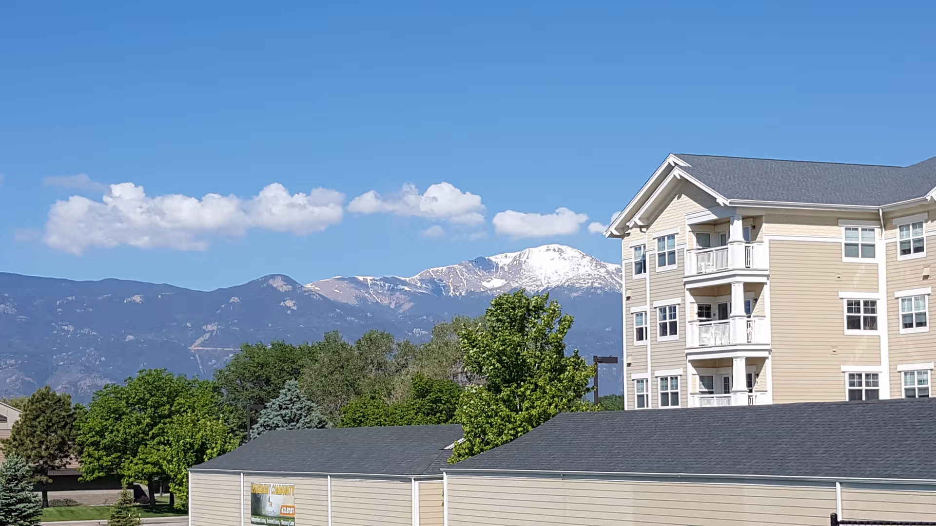 Exterior view of a beige multi-story senior living building with balconies and mountains in background.
