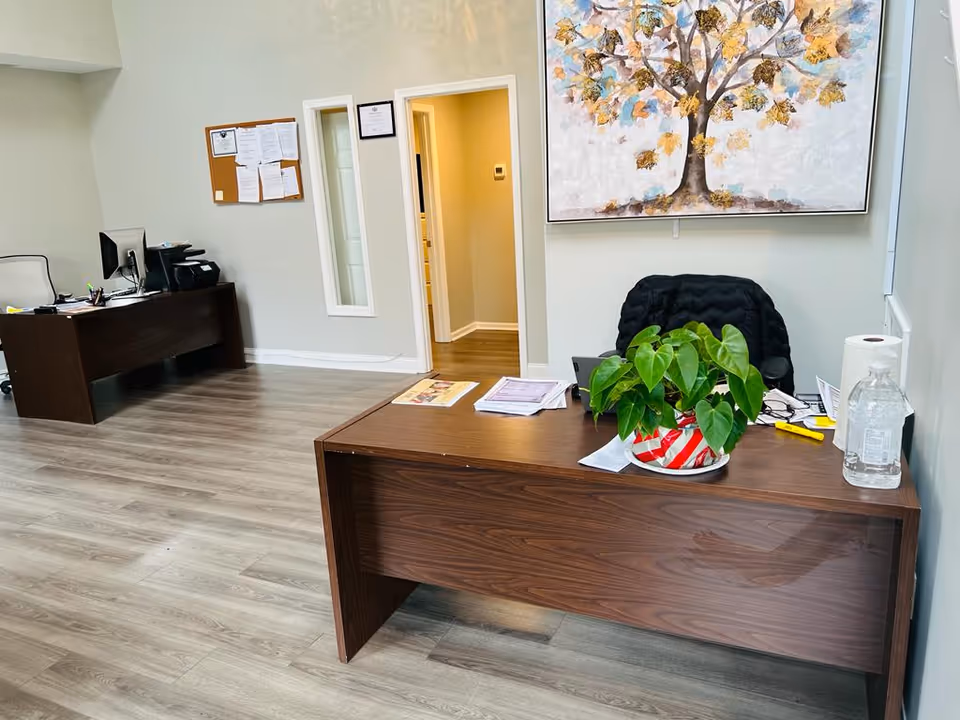 Reception area with a wooden desk, plant, water bottle, and a large tree painting.