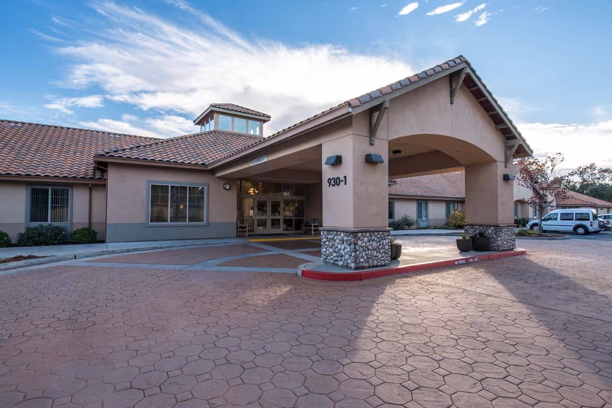 Front entrance of Meadow Oaks of Roseville with covered drive, tan building, stone pillars.
