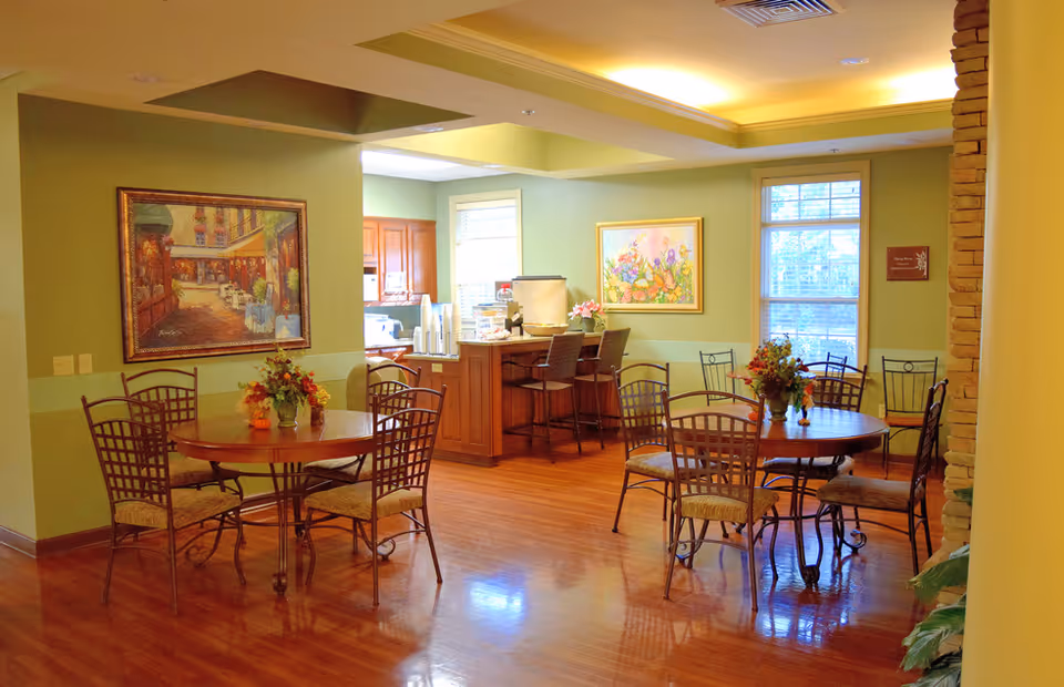 Cozy dining area with round tables, metal chairs, and artwork on green walls.