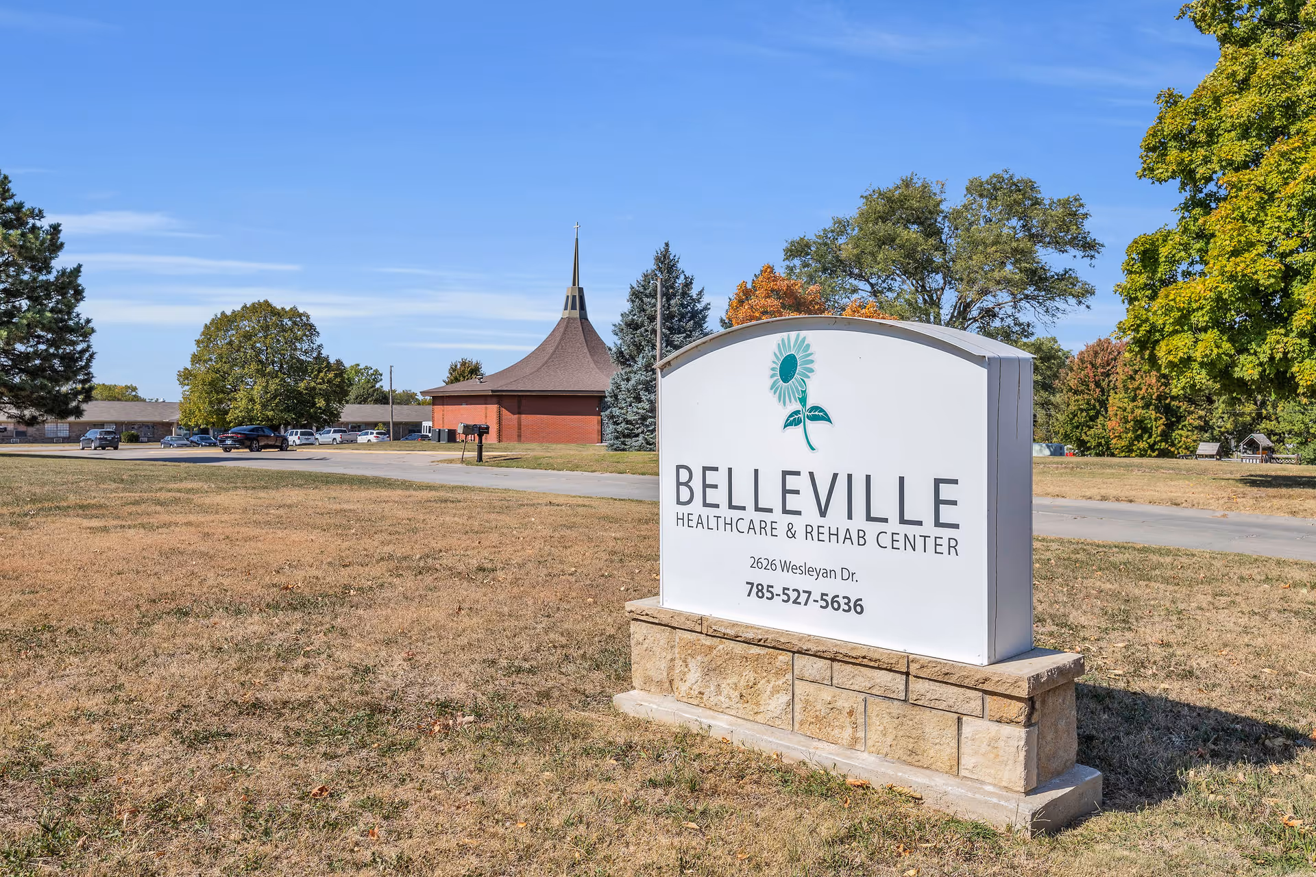 Outdoor view of the Belleville Healthcare & Rehab Center sign on a grassy lawn with the facility building and trees in the background.