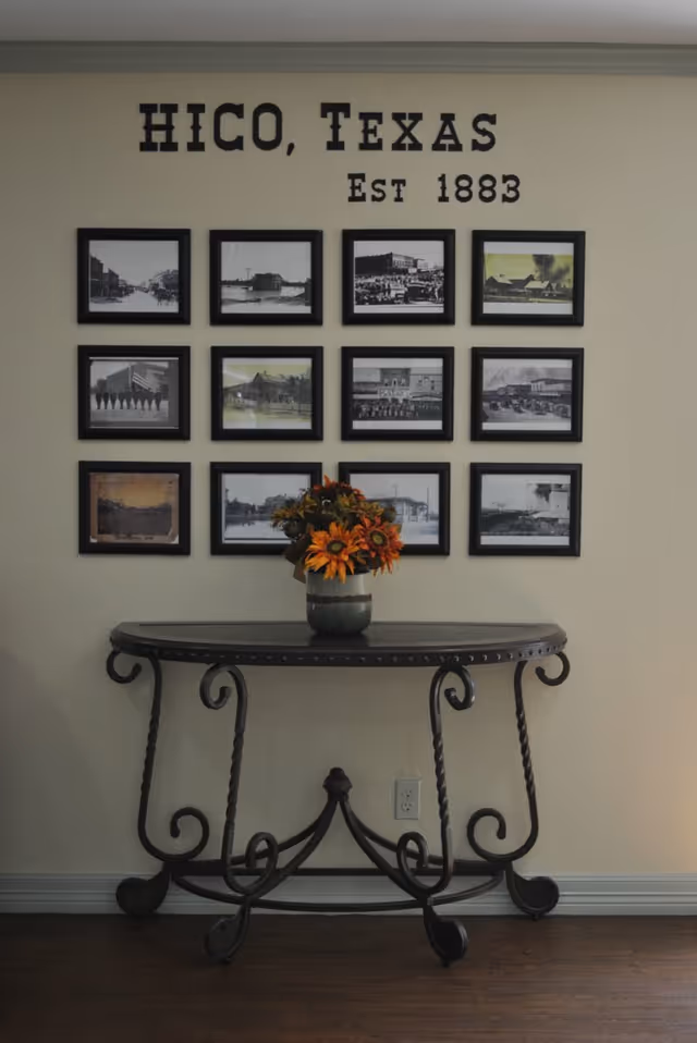 Interior hallway with a grid of framed photos titled HICO, Texas, and a floral console table.