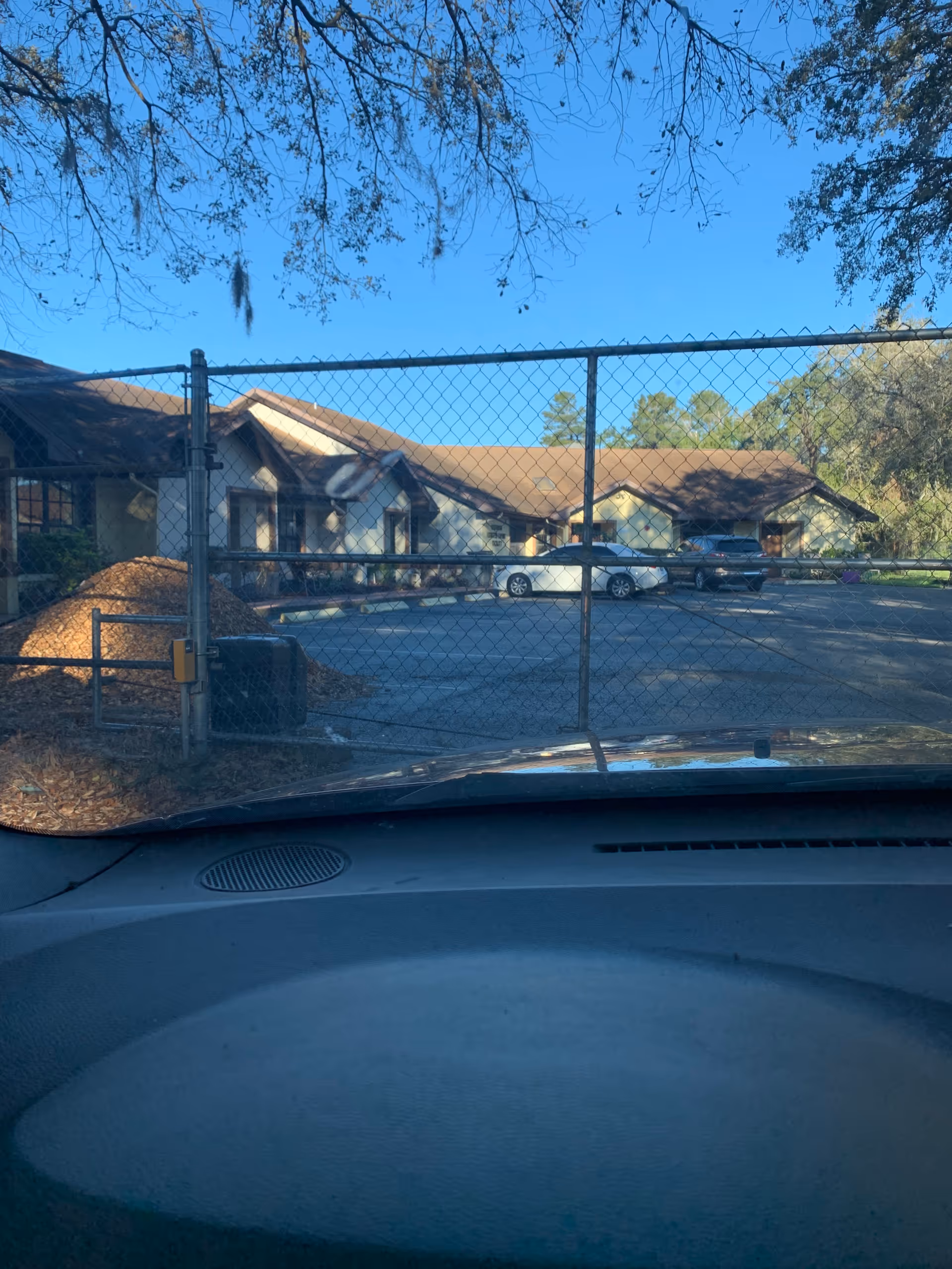 View from a car shows a chain-link gate and single-story senior living buildings beyond.
