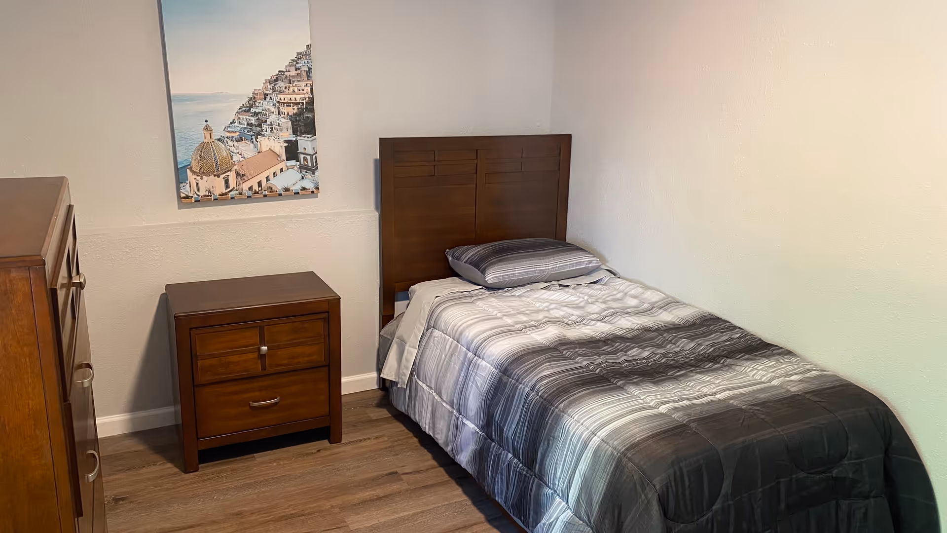 A small bedroom with a single bed, wooden headboard, dresser, and nightstand.