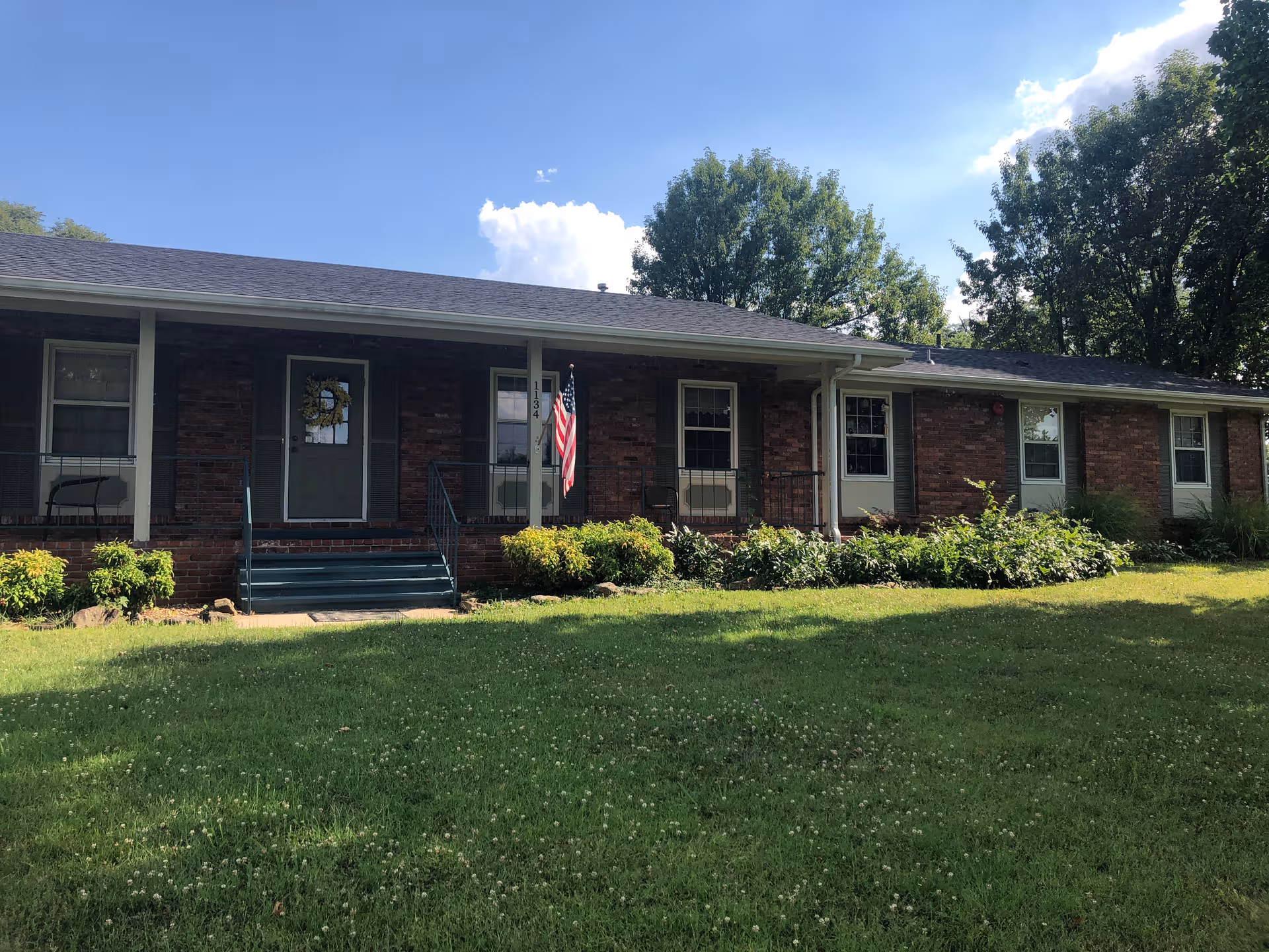 Brick, single-story building with a front porch, steps, flag, and manicured lawn.