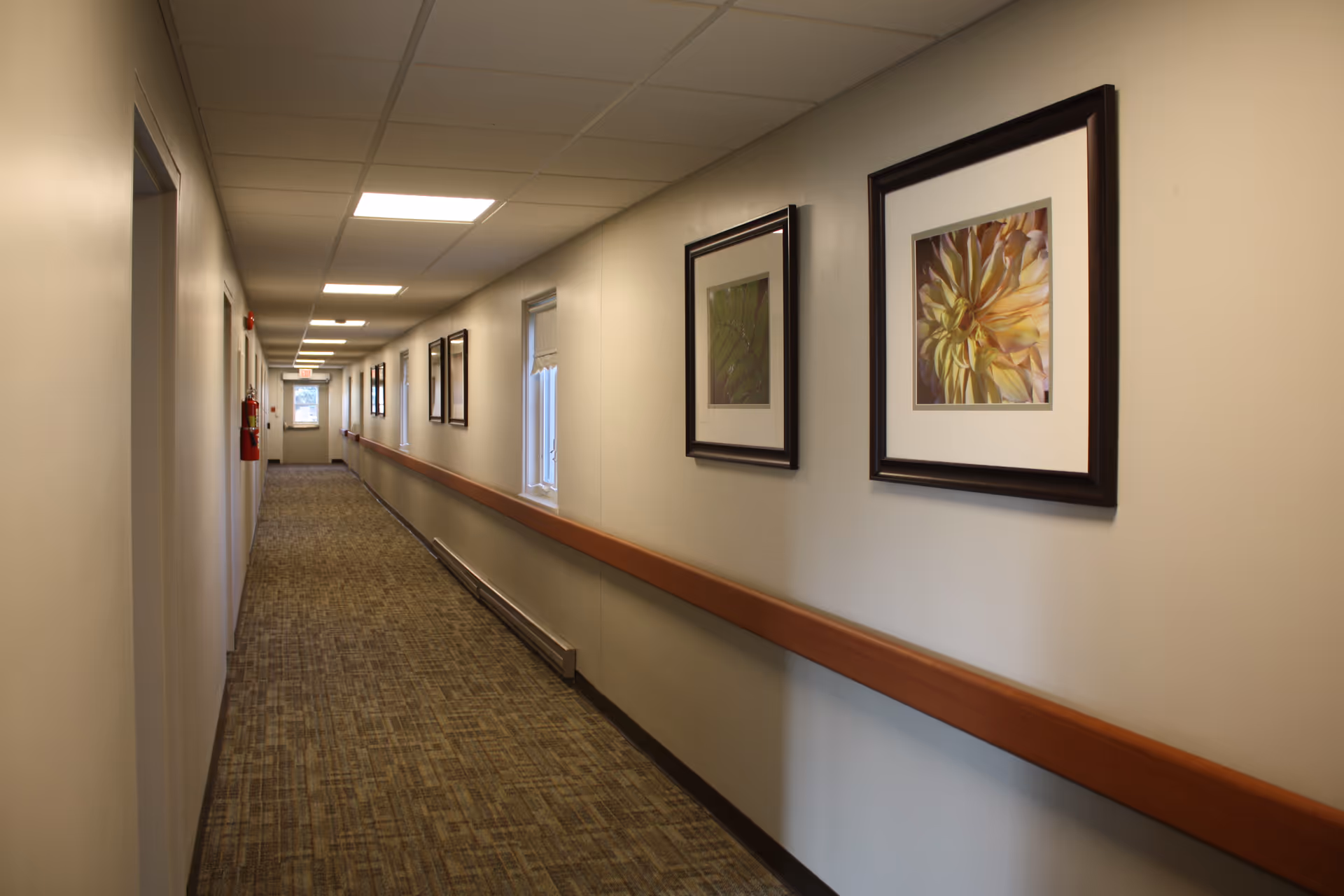 Long hallway in a senior living facility with framed artwork along the walls.