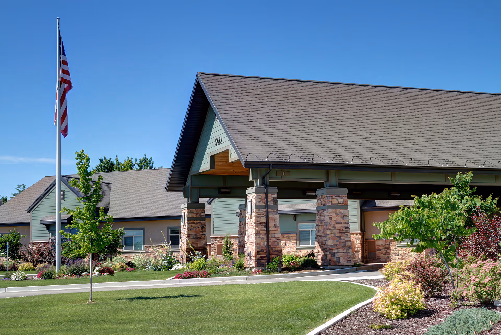 Exterior view of a senior living facility entrance with flagpole and landscaping.