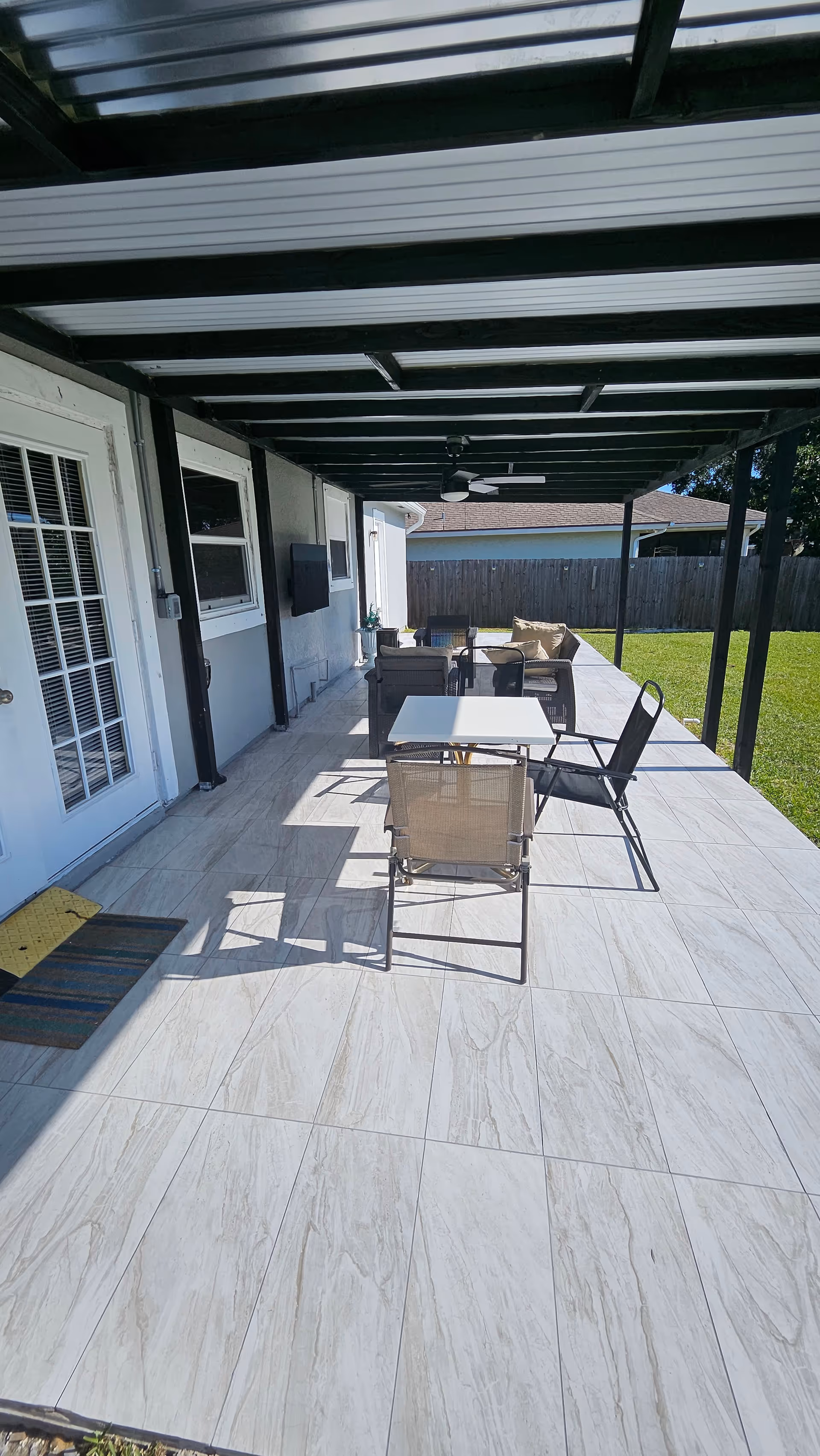 Covered outdoor patio with seating and a table beside a house