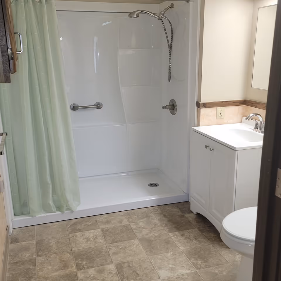Compact bathroom featuring a walk-in shower, sink vanity, toilet, and pale green curtain.
