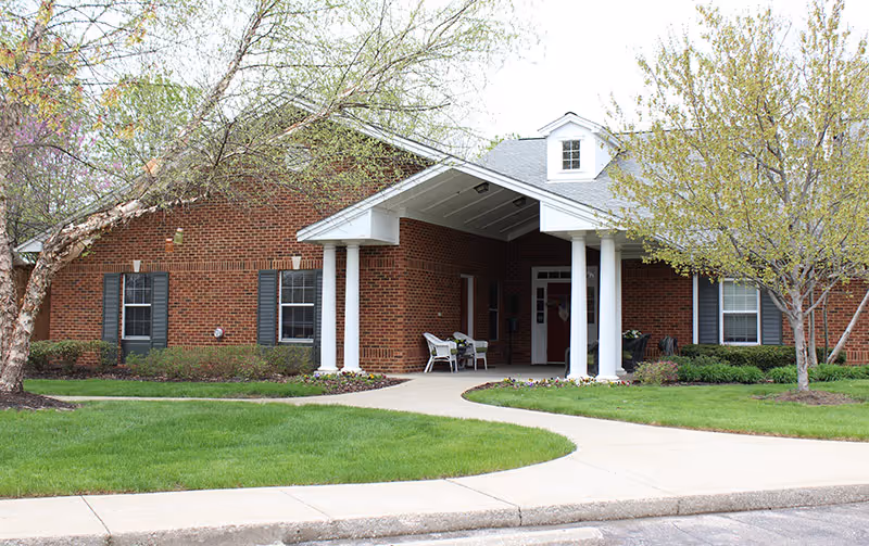 Brick senior living facility exterior with a covered entrance and chairs on the porch.