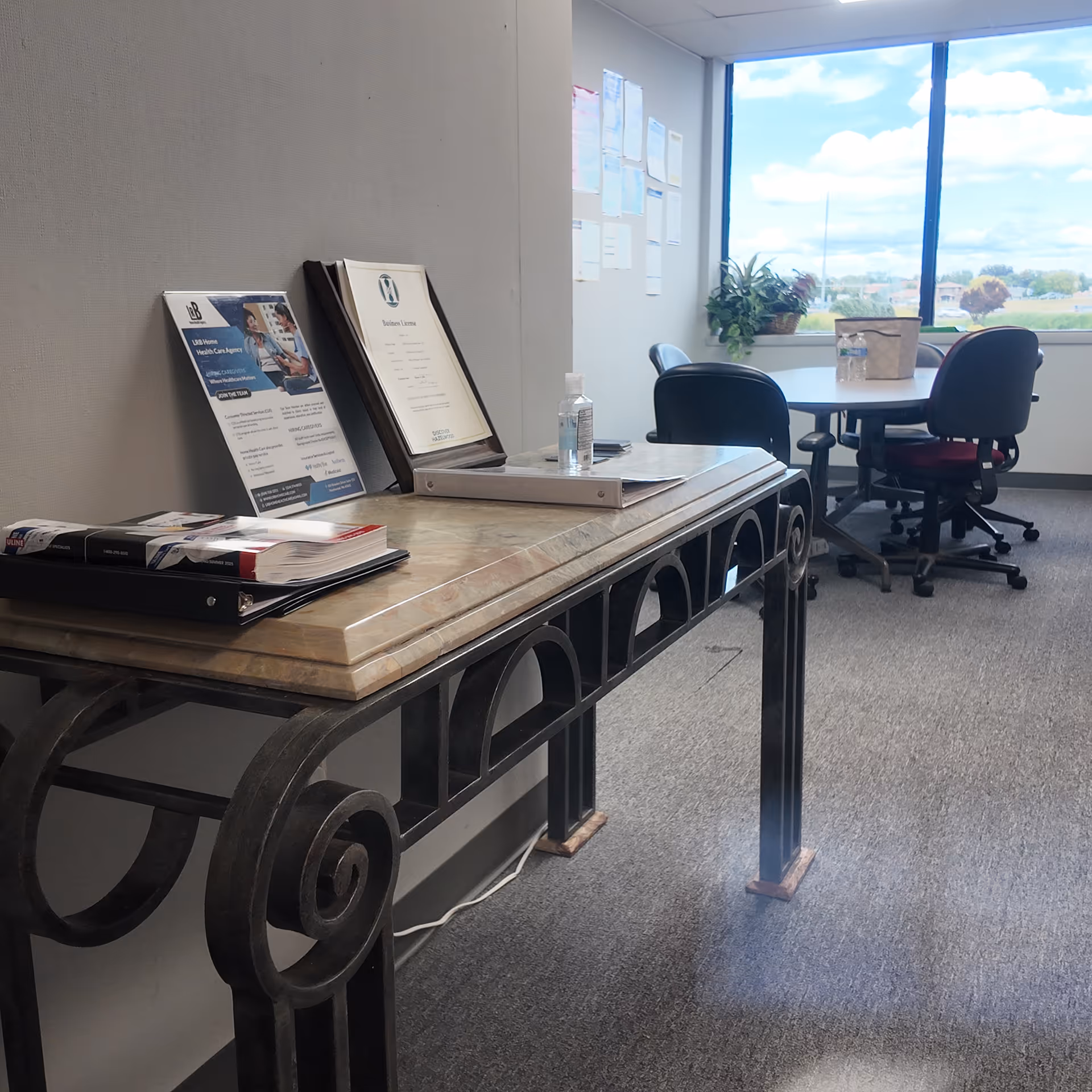 Marble reception desk with brochures and sanitizer, near a round table by a large window.