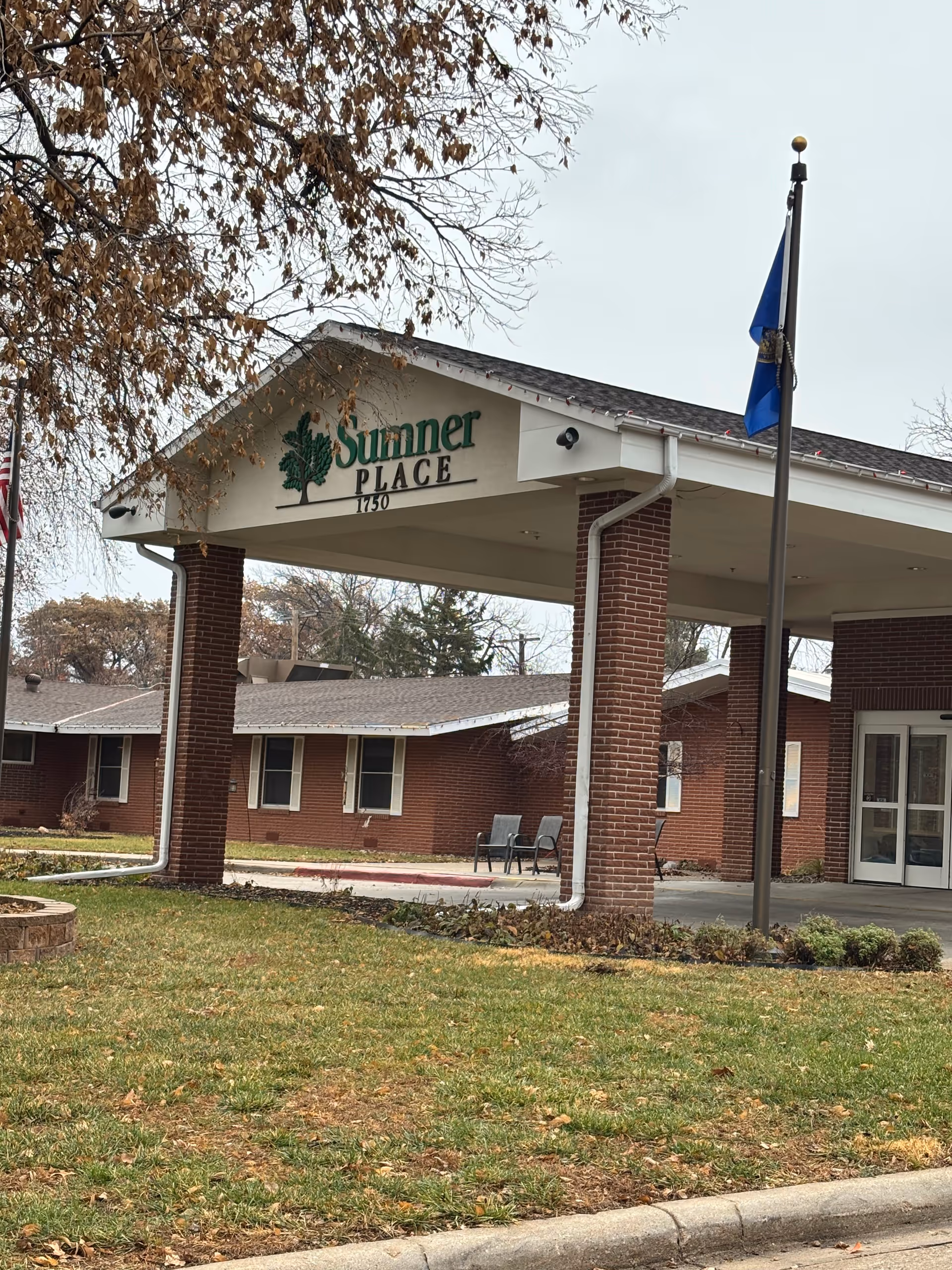 Brick facility entrance with a covered walkway, 'Summer Place' sign, and chairs outside.