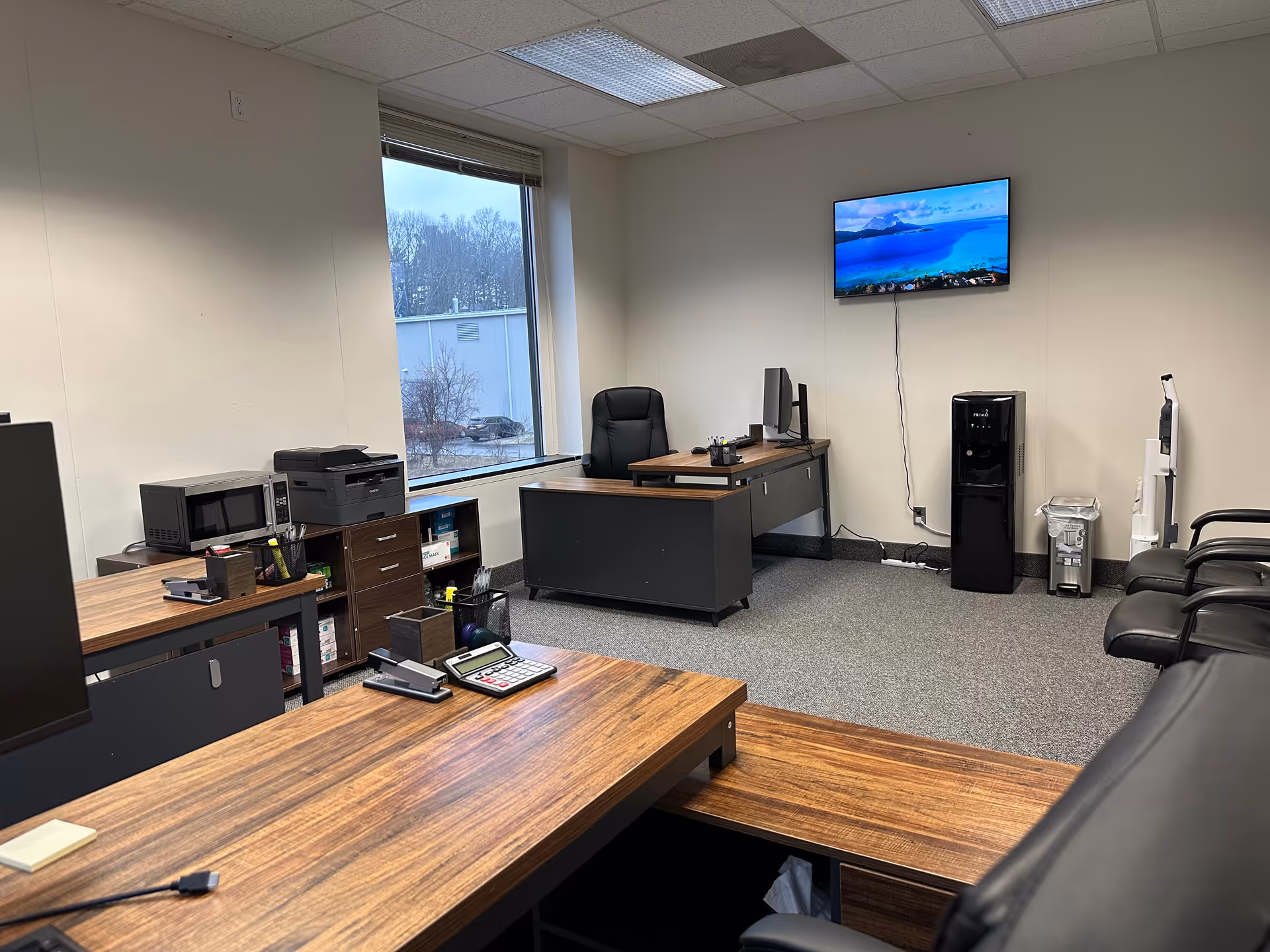 Office inside a healthcare facility with desks, computer, printer, and a wall-mounted TV.