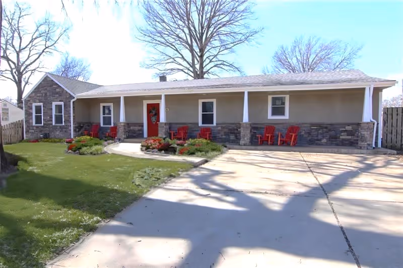 Front view of a single-story senior living facility with red chairs on the porch.