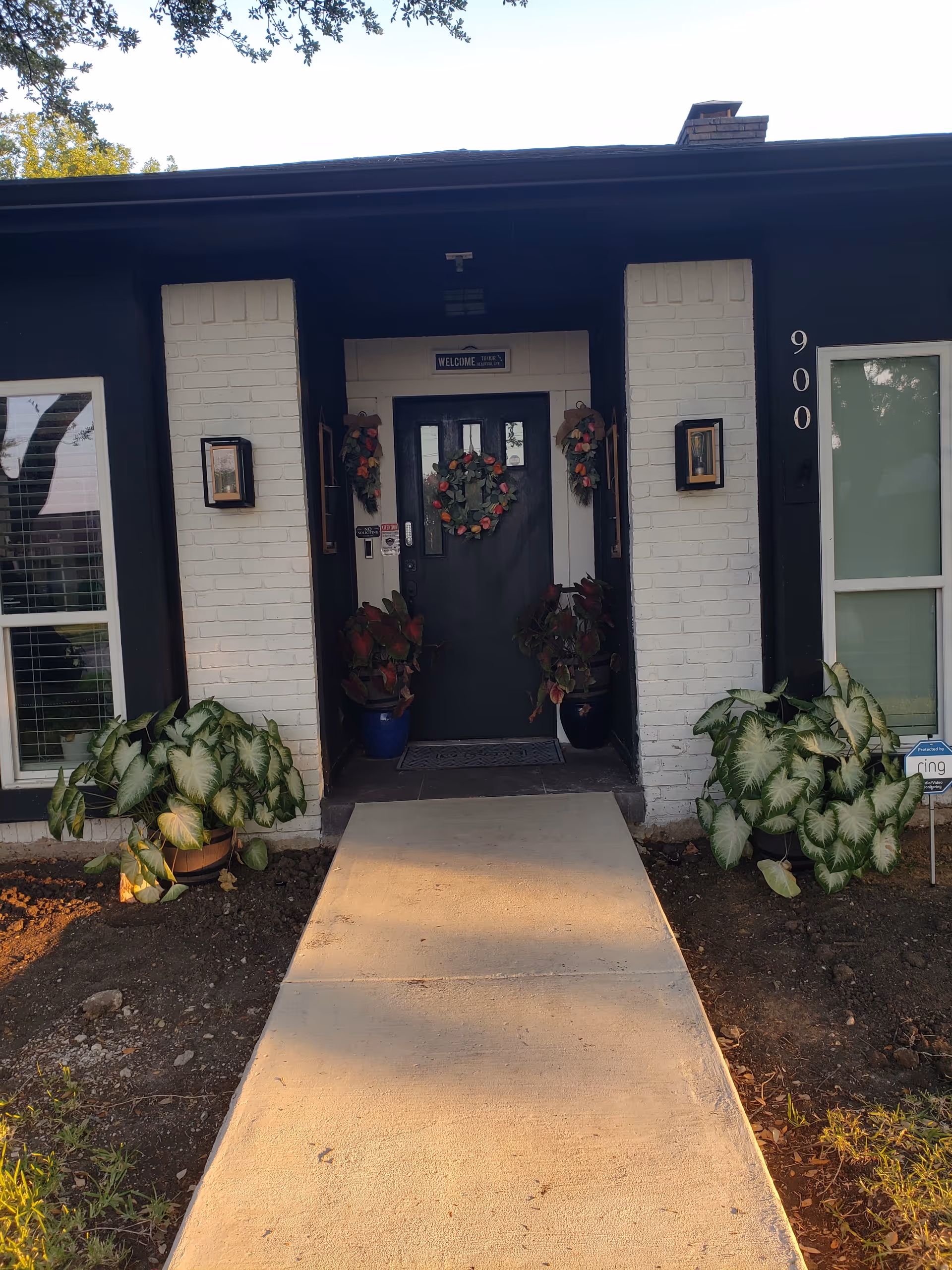 Front entrance of a building with wreaths, potted plants, and a concrete walkway.