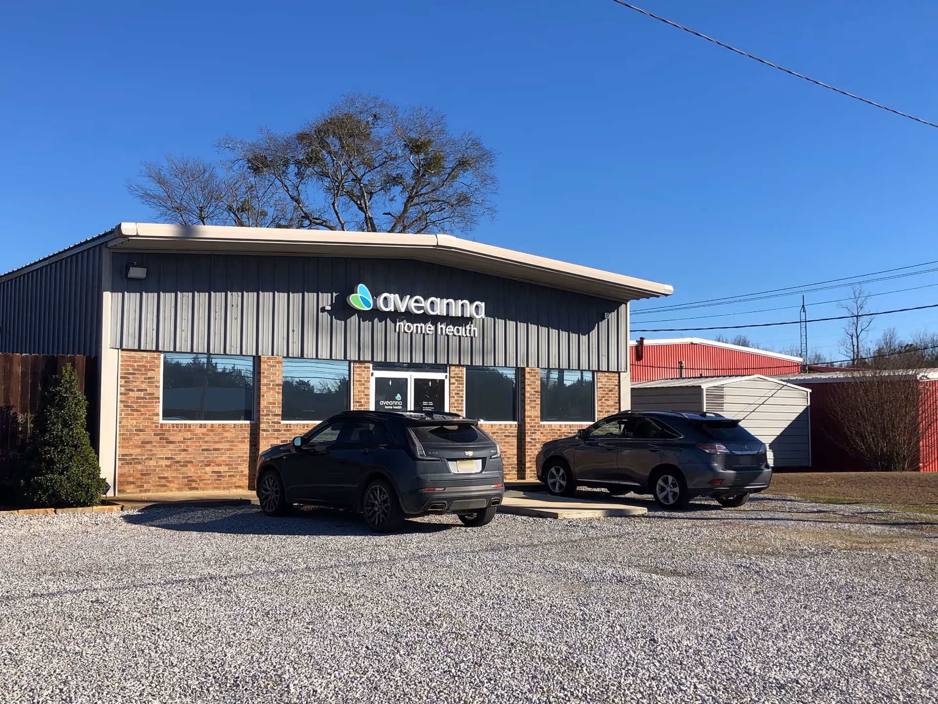 Front view of Aveanna Home Health building with two parked SUVs in a gravel lot.