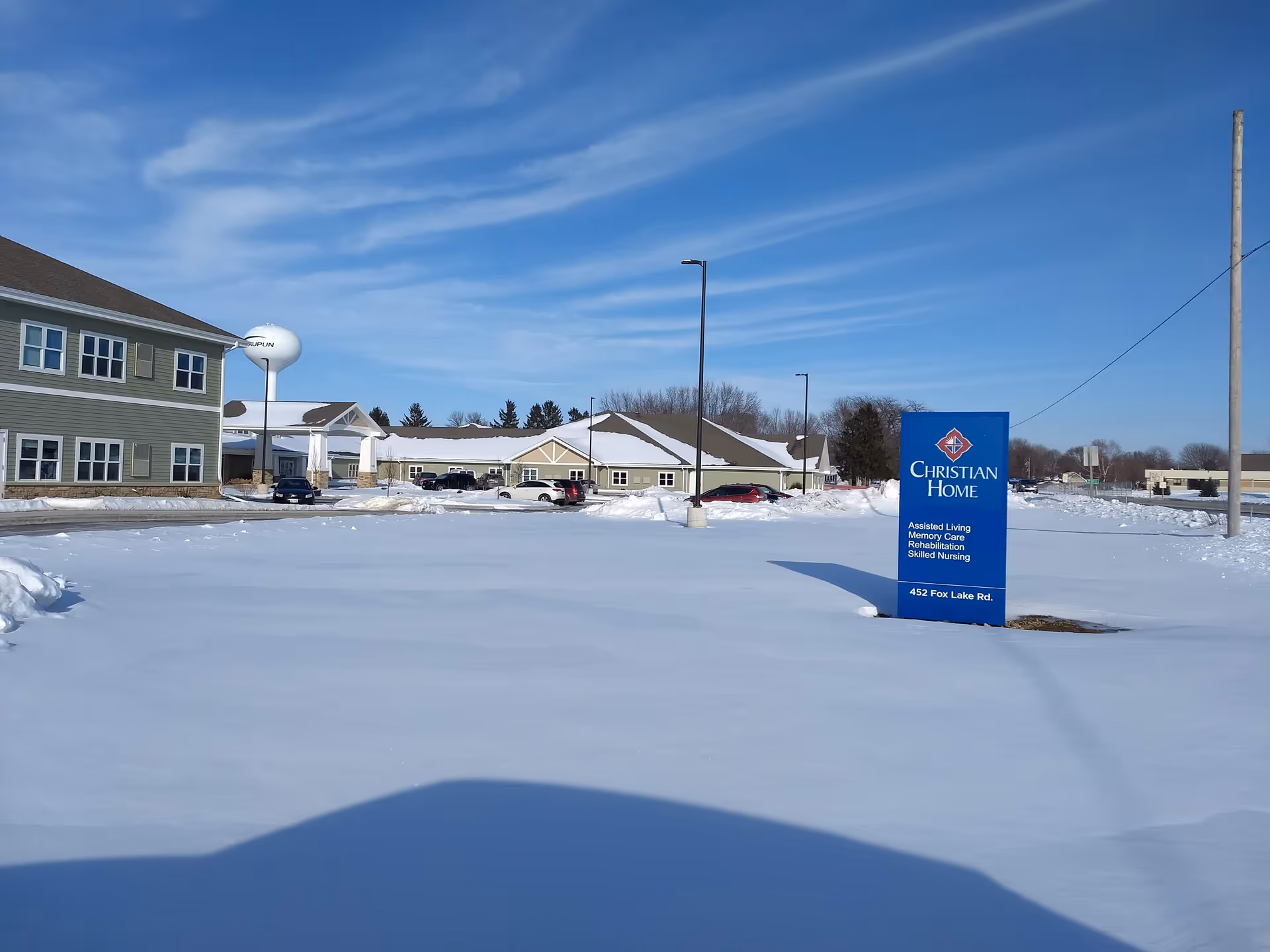 Snow-covered parking lot and front of Christian Home and Rehabilitation Center with blue sign.