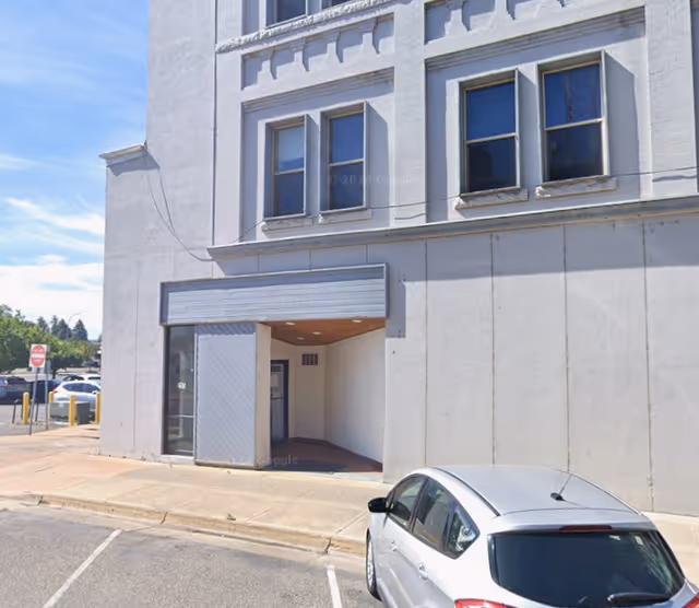 Urban building facade with a covered entrance, sidewalk, and a parked silver car.