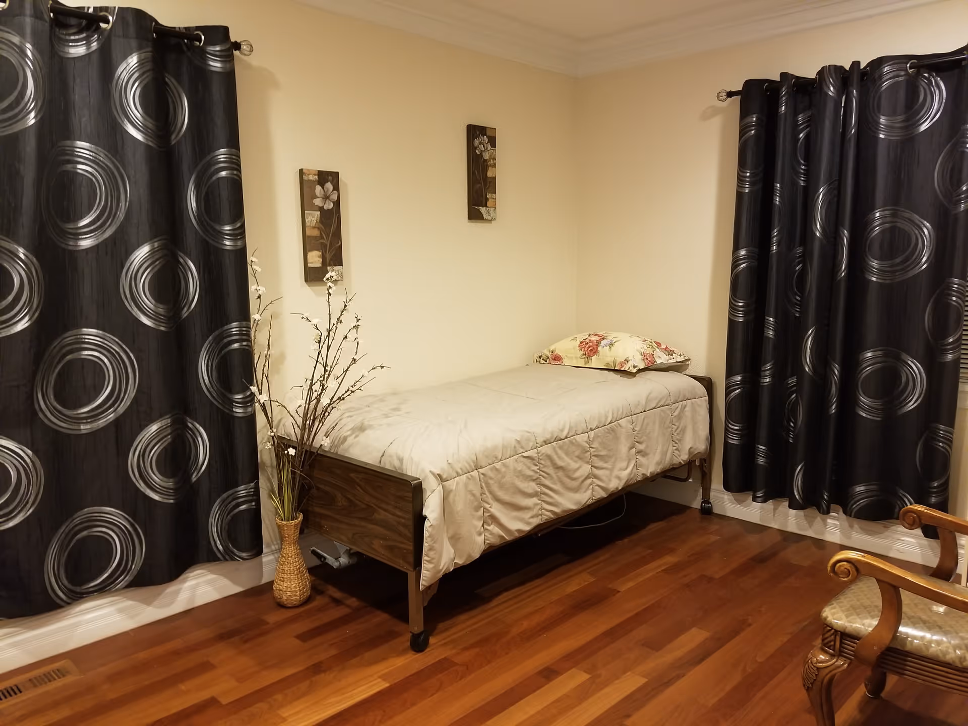 A small furnished bedroom with a single bed, curtains, and decorative wall art.