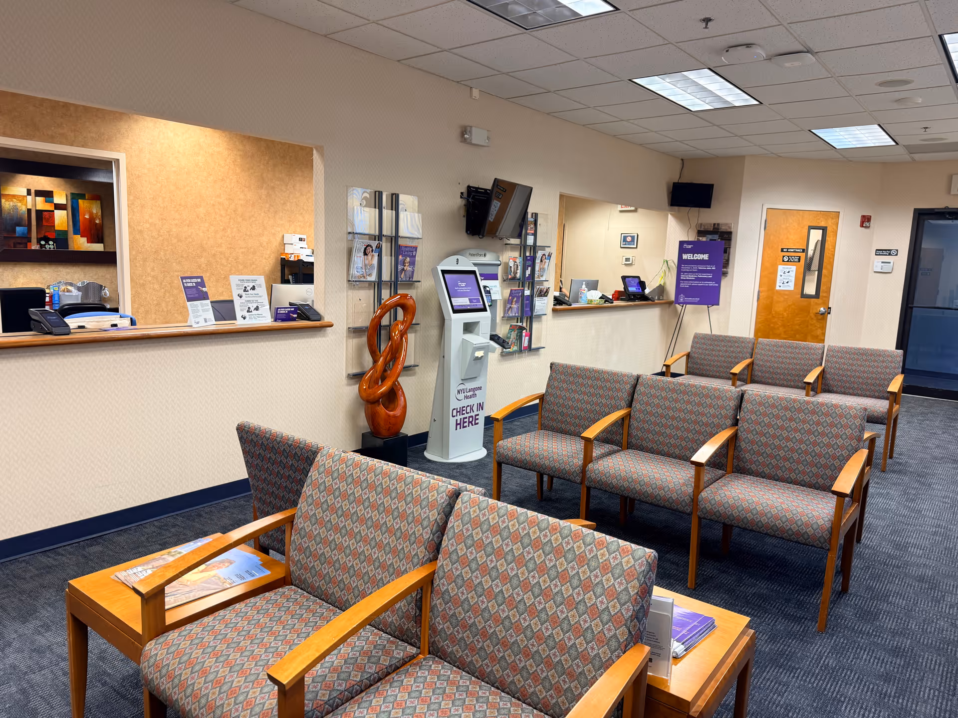 Lobby area with patterned chairs, reception window, and a self check-in kiosk.