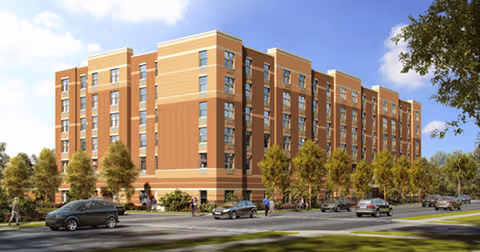 Exterior view of a multi-story brick senior living building with trees and cars along the street.