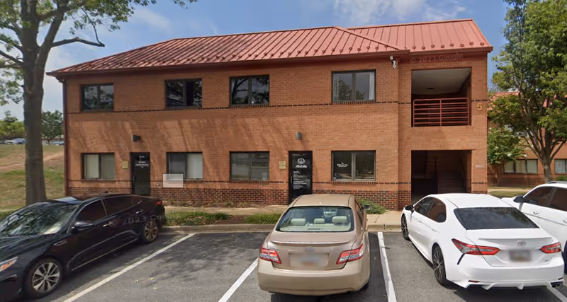 Two-story brick building with a red metal roof and several cars in the front parking lot.