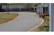 A curved driveway leads to a single-story senior living building with front porches and landscaping.