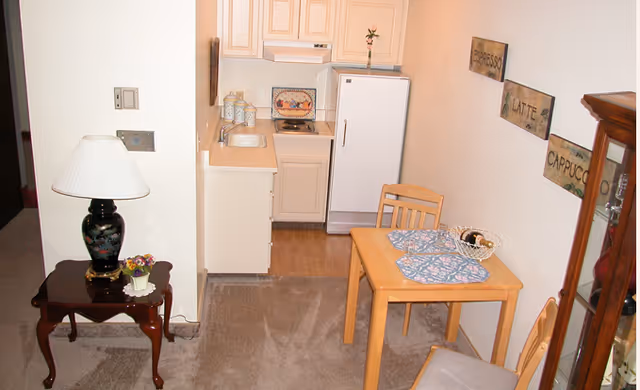 Cozy kitchenette and dining nook in a small apartment with table, chairs, and fridge.
