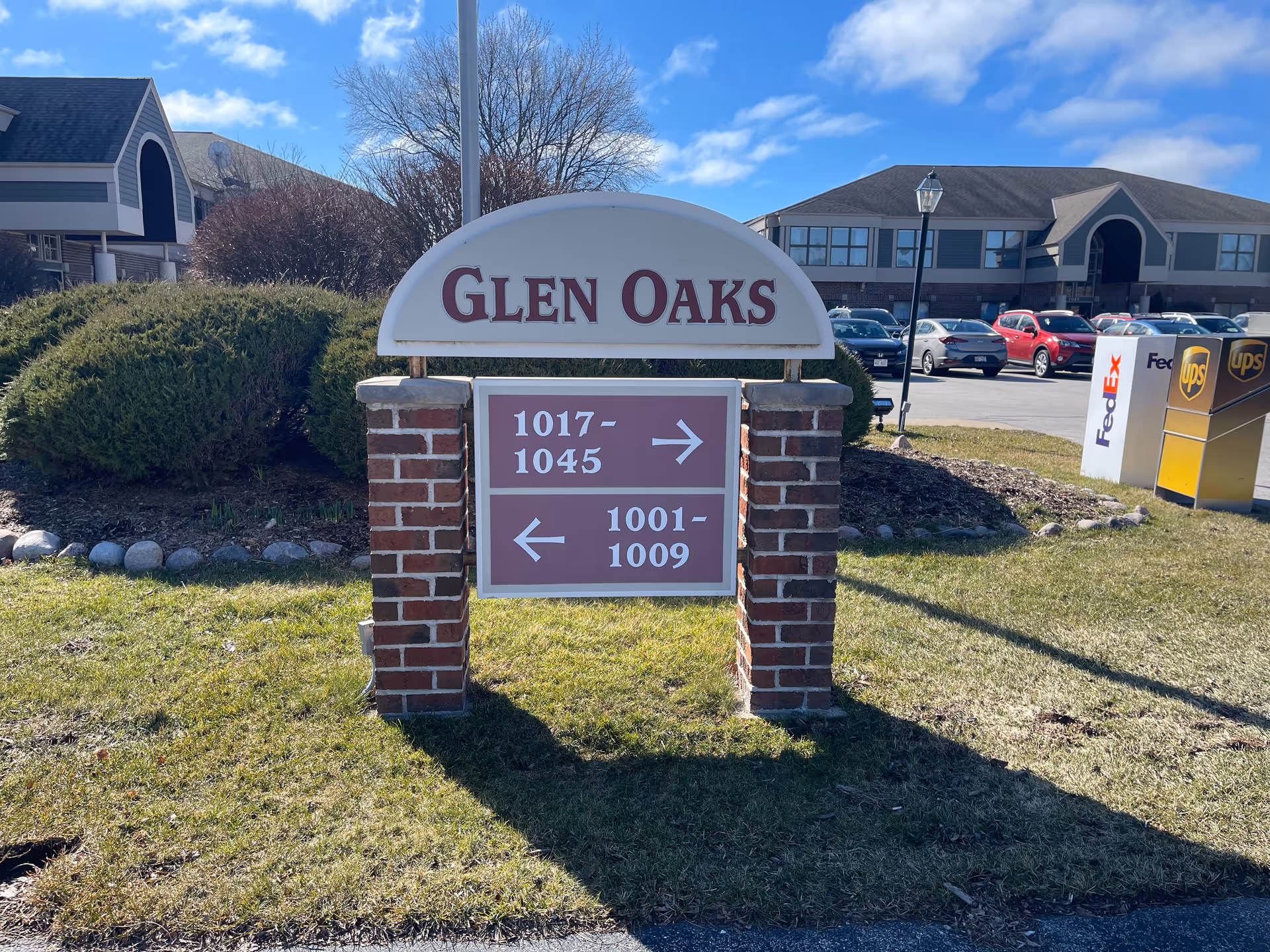 Exterior view of a senior living facility sign reading GLEN OAKS with buildings and parked cars