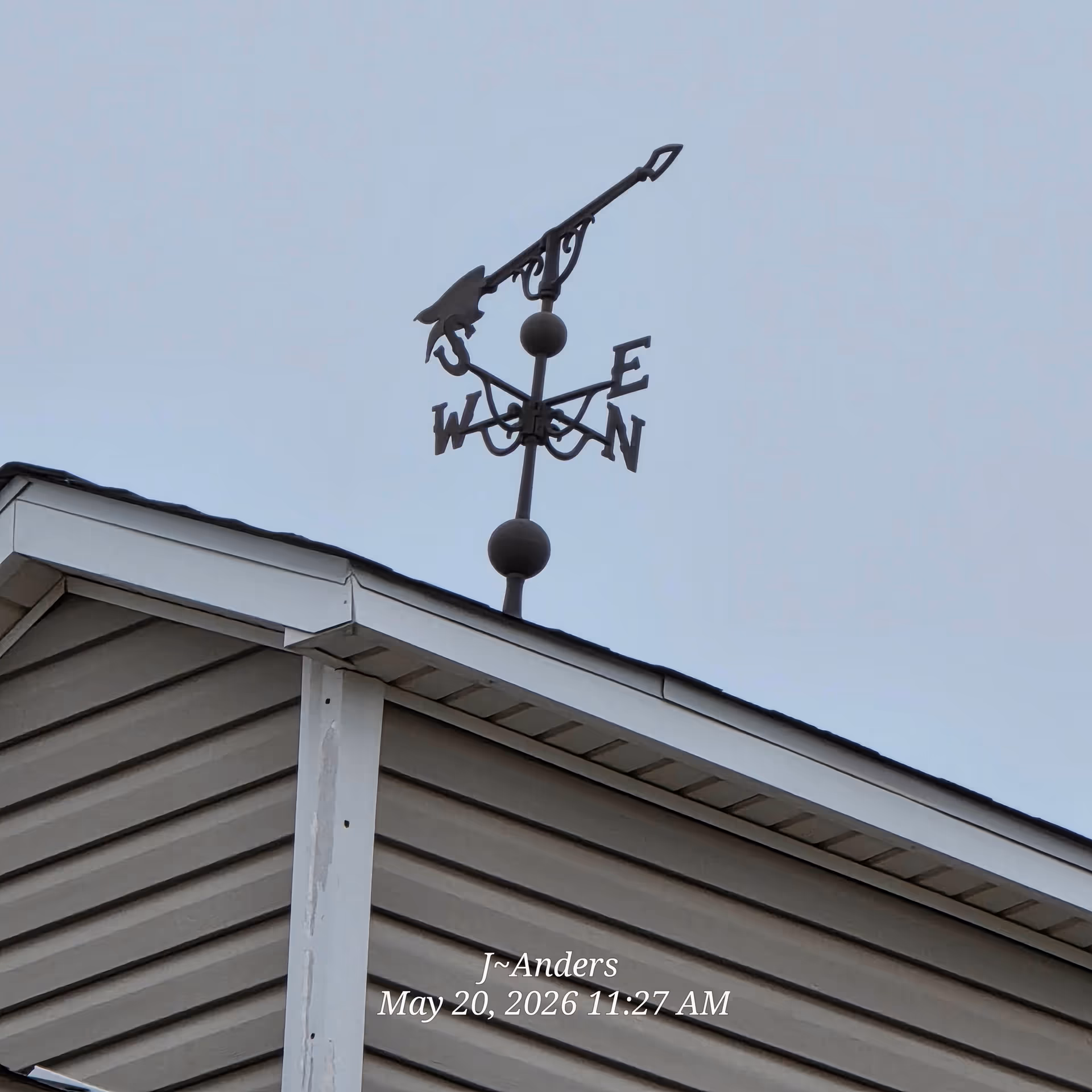 Weather vane atop a sloped roof against a clear blue sky.