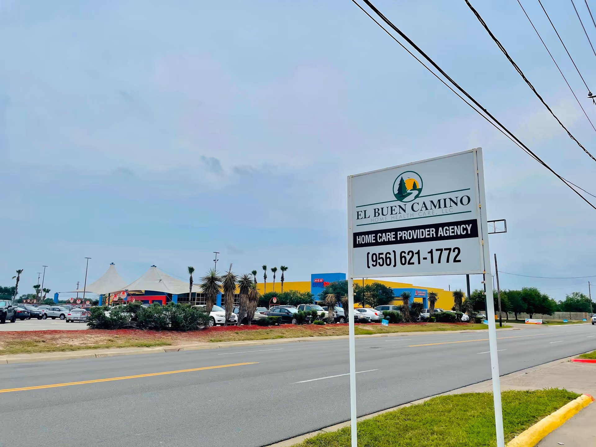 Outdoor sign for El Buen Camino Home Health Care, with parking lot and building in background.