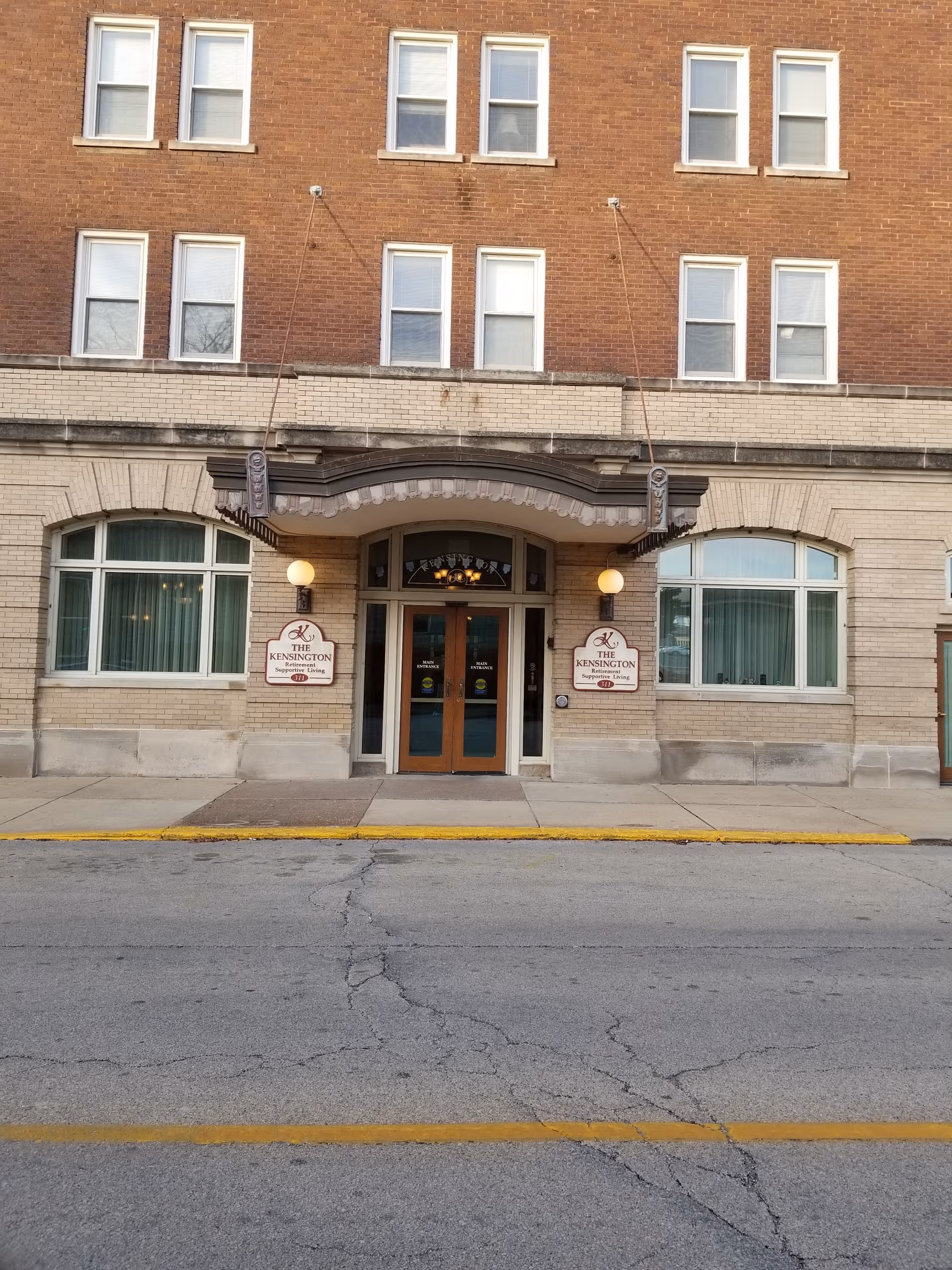 Brick building with The Kensington entrance, arched doorway, and street in foreground.