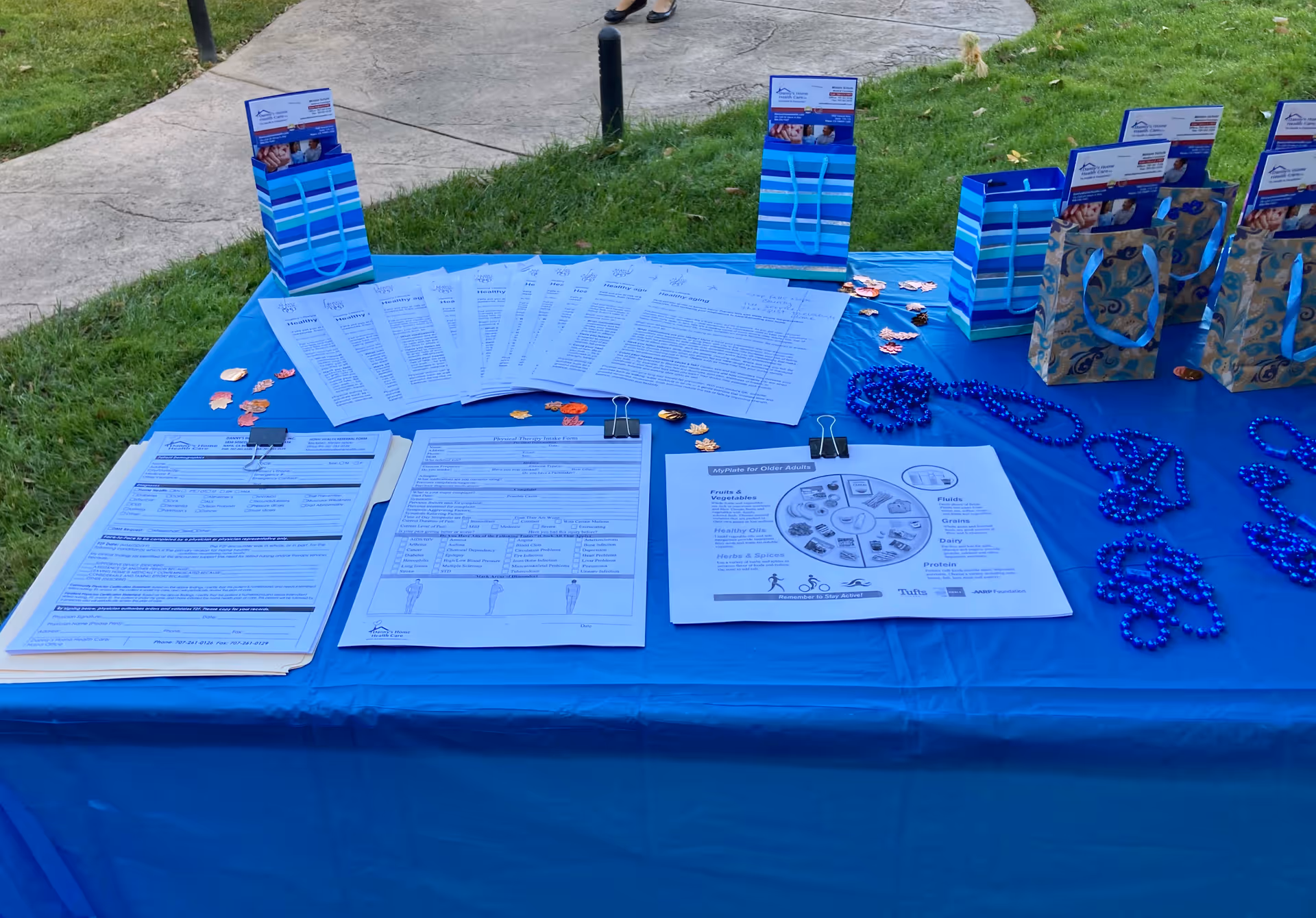 Blue table on lawn displays forms, brochures, and gift bags at a health fair.