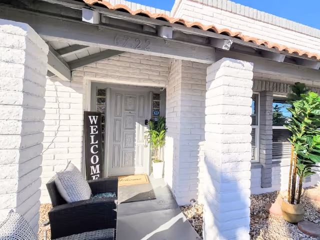 White brick entrance with a vertical welcome sign, seating, and potted plants at the front.