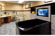 Accessible bathroom in a senior living facility with sink, toilet, tiled walls, and a black tub.