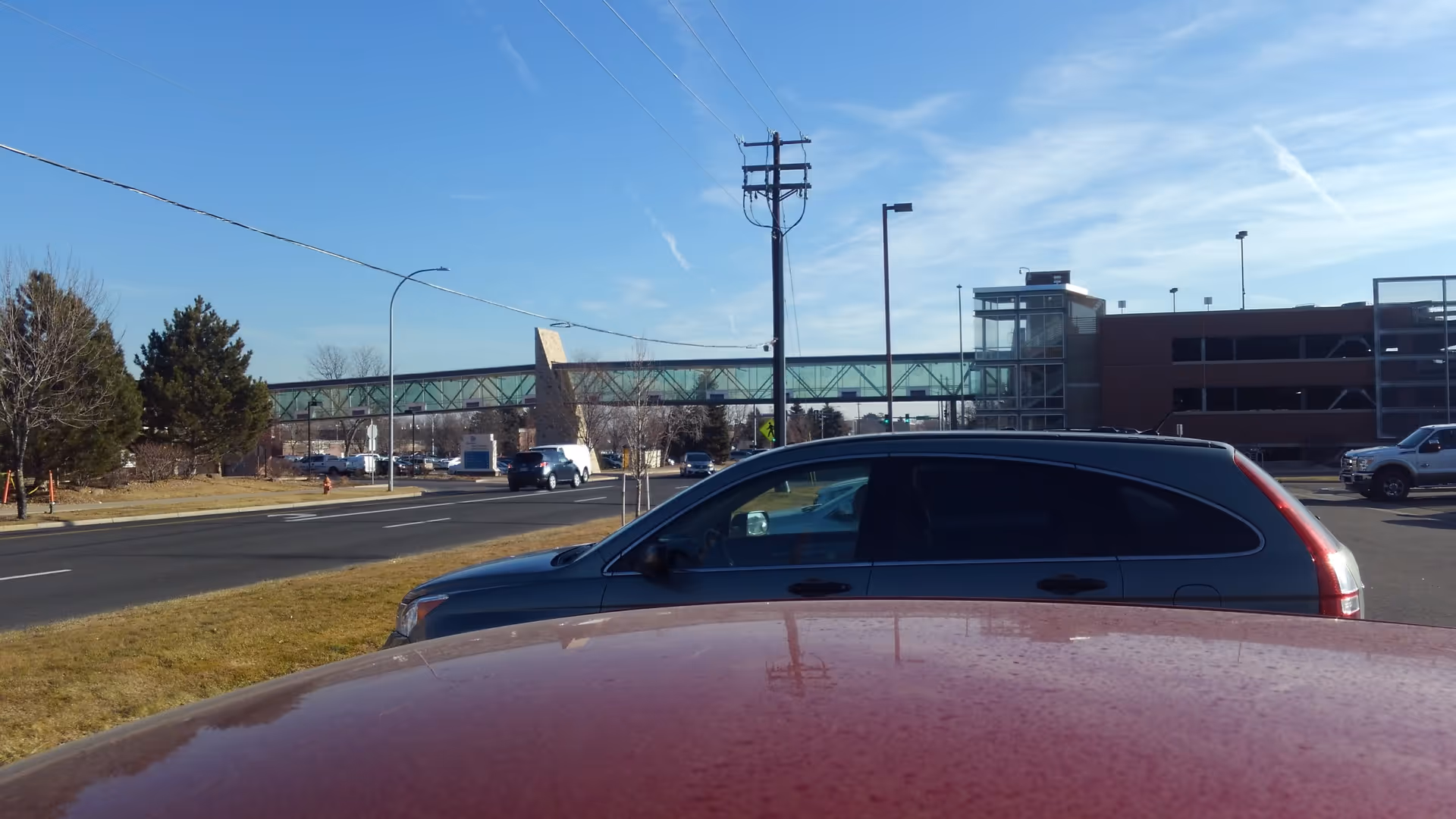 Exterior view of a hospital campus with parking lot, blue sky, and skybridge.