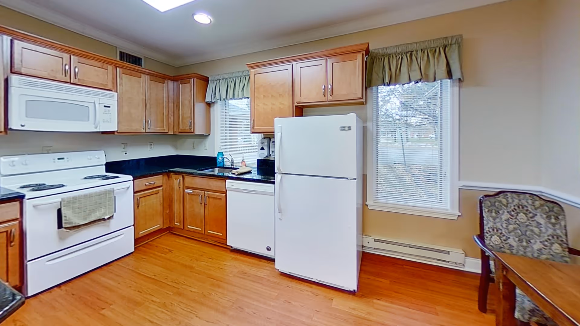 Bright kitchen with white appliances, wooden cabinets, black countertops and hardwood floors.