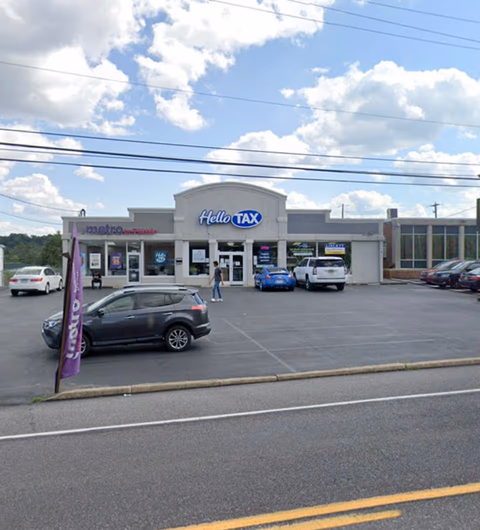 Front of a strip plaza with Hello TAX sign and parked cars.