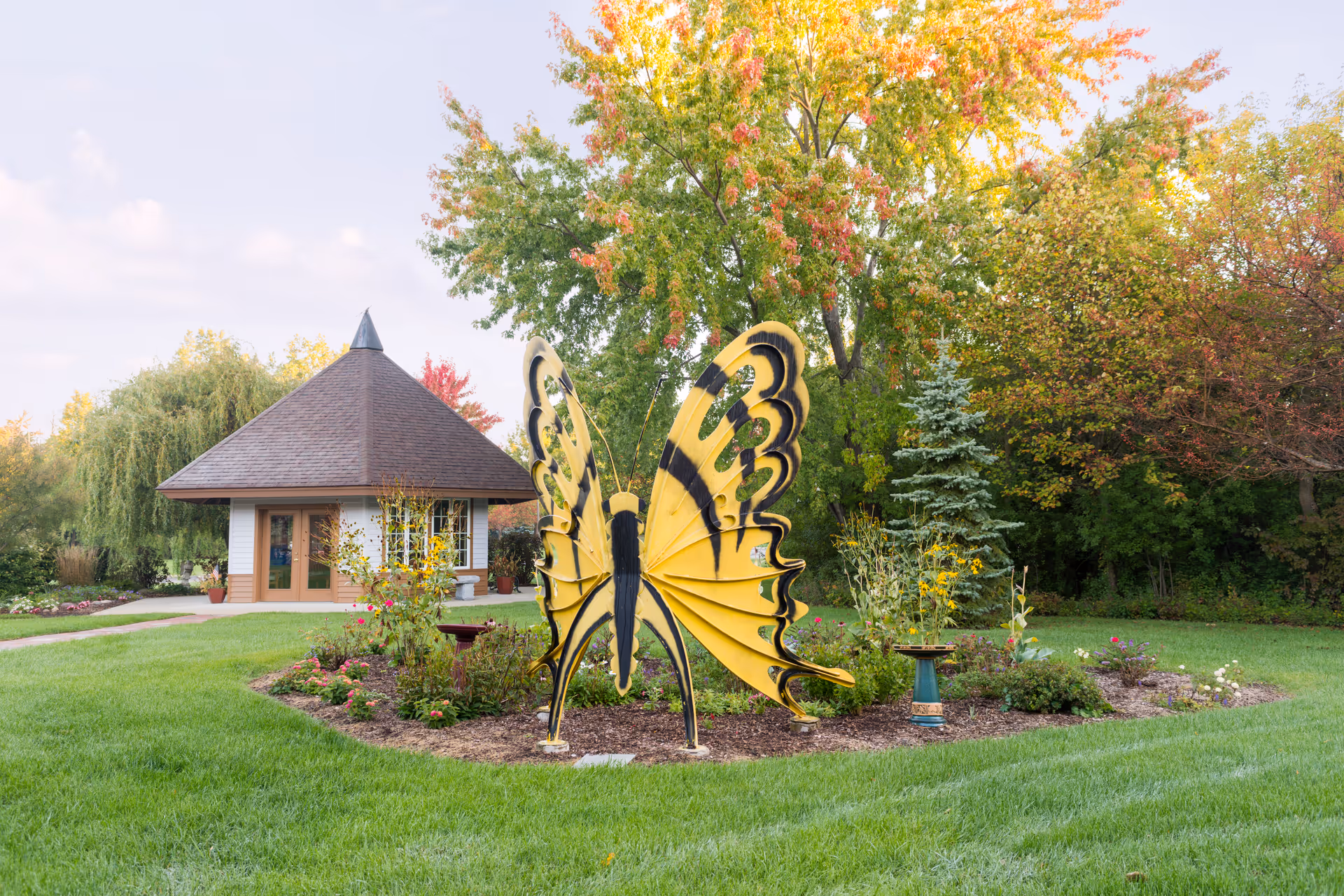Butterfly sculpture in a manicured hospice garden with a small pavilion and trees.