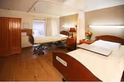 A spacious shared bedroom in a senior care facility with two beds and furniture.