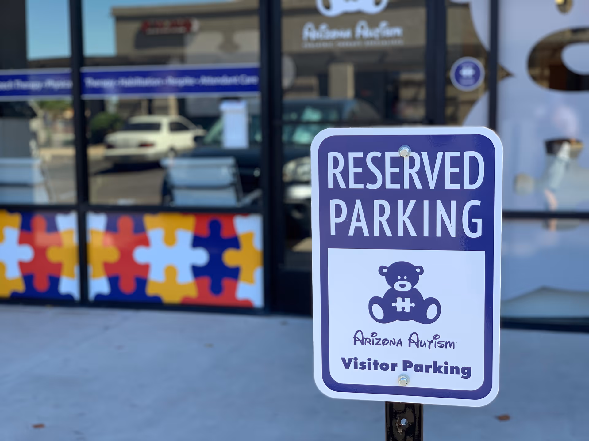 Blue Reserved Parking sign for Arizona Autism outside a glass-front facility.