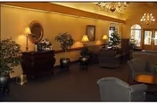 Warm interior lounge in a senior living facility with sofas, lamps, and potted plants.